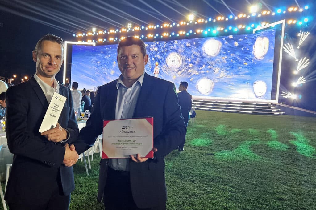 Reynardt Badenhorst, Managing Director of NZTeco, and Marius Thesner, Financial Director of NZTeco, proudly receiving the ZKTeco Premier Rapid Breakthrough Award 2024, presented on stage with an illuminated backdrop at a ZKTeco event.