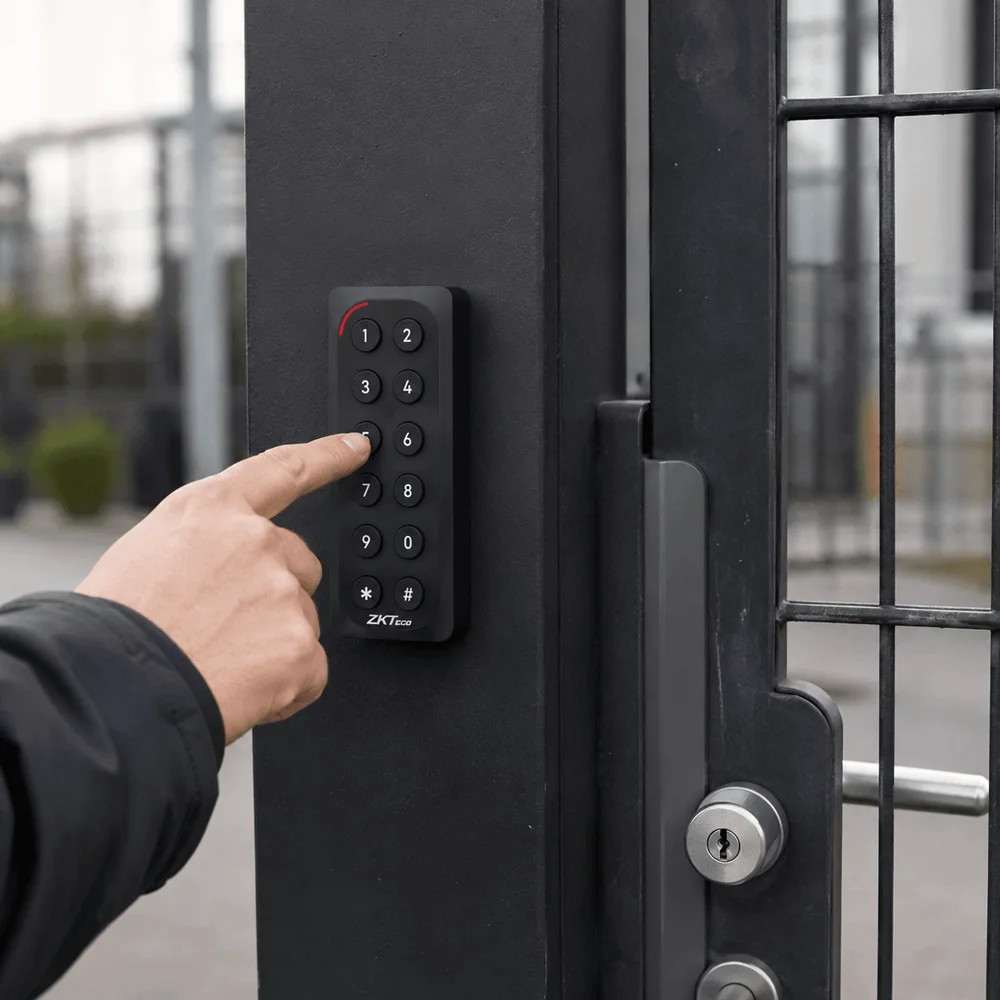 A finger pressing a numbered button on a ZKTeco KR902 keypad reader